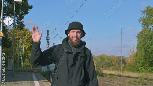 Young man with a beard waving his hands in greeting at the railway station