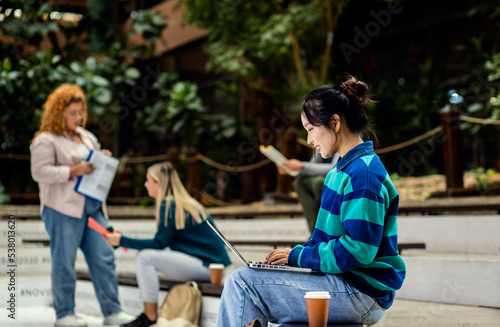 Portrait of female student siting in campus using laptop.