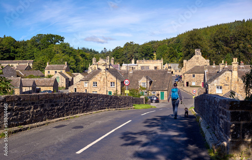 A hiker crossing a bridge into the small traditional rural village of Blanchland on a sunny autumn day in Northumberland on the border of County Durham, England, UK. photo