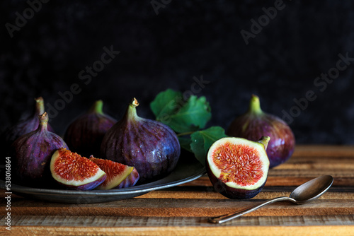 Fresh fig fruits in a vintage metal plate with cut pieces with a spoon against vintage background - dark and moody photography