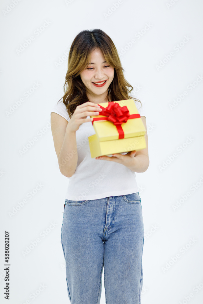 Isolated cutout studio shot Millennial Asian young happy surprise shocked female model in casual outfit standing smiling holding opening red ribbon yellow wrapped present gift box on white background Isolated cutout studio shot Millennial Asian young happy surprise shocked female model in casual outfit standing smiling holding opening red ribbon yellow wrapped present gift box on white background