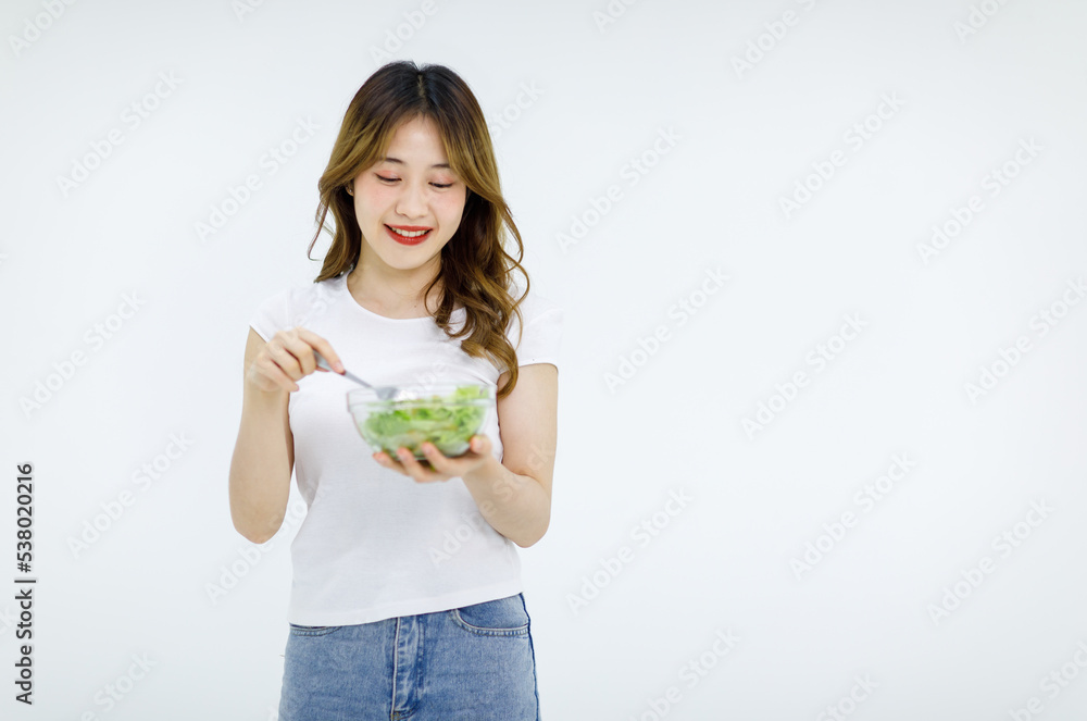 Isolated cutout studio shot of Millennial Asian young happy female teenager model in casual outfit standing smiling holding fresh organic salad glass bowl and red tomato on fork on white background Isolated cutout studio shot of Millennial Asian young happy female teenager model in casual outfit standing smiling holding fresh organic salad glass bowl and red tomato on fork on white background