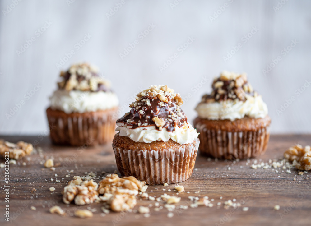 Tasty chocolate muffin with creme mascarpone and chocolate on top, covered with nuts. Placed on wooden desk. Sweet fresh and homemade cupcake. Tasty chocolate muffin with creme mascarpone and chocolate on top, covered with nuts. Placed on wooden desk. Sweet fresh and homemade cupcake.