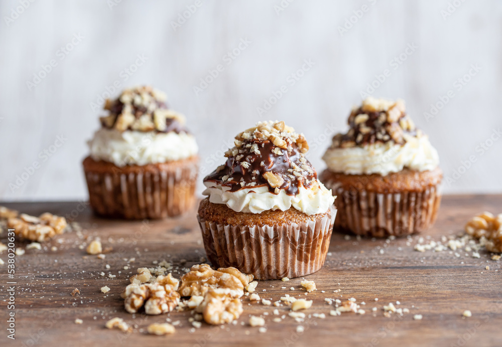 Tasty chocolate muffin with creme mascarpone and chocolate on top, covered with nuts. Placed on wooden desk. Sweet fresh and homemade cupcake. Tasty chocolate muffin with creme mascarpone and chocolate on top, covered with nuts. Placed on wooden desk. Sweet fresh and homemade cupcake.