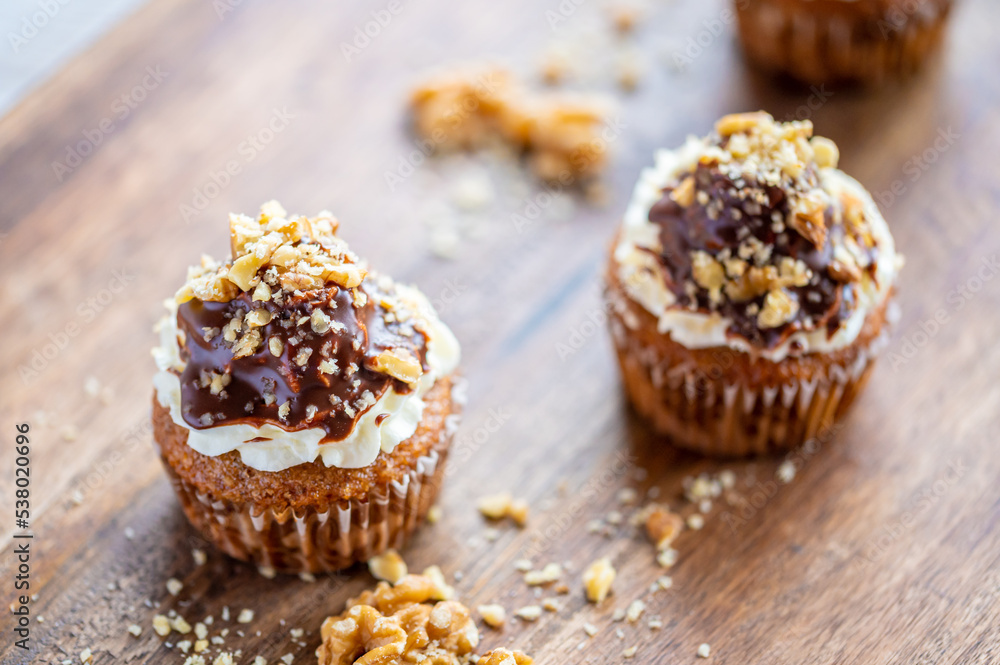 Tasty chocolate muffin with creme mascarpone and chocolate on top, covered with nuts. Placed on wooden desk. Sweet fresh and homemade cupcake. Tasty chocolate muffin with creme mascarpone and chocolate on top, covered with nuts. Placed on wooden desk. Sweet fresh and homemade cupcake.