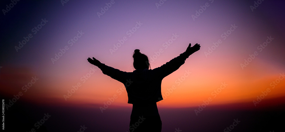 Silhouette of cheering hiking woman open arms to the sunrise stand on mountain