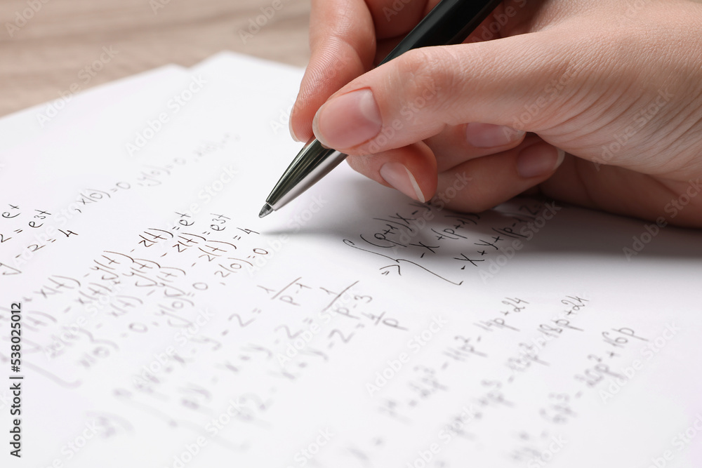 Student writing different mathematical formulas on paper, closeup