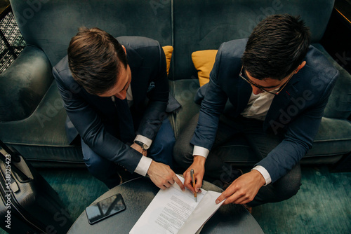 High angle view of businessman signing contract sitting by colleague at hotel lounge photo