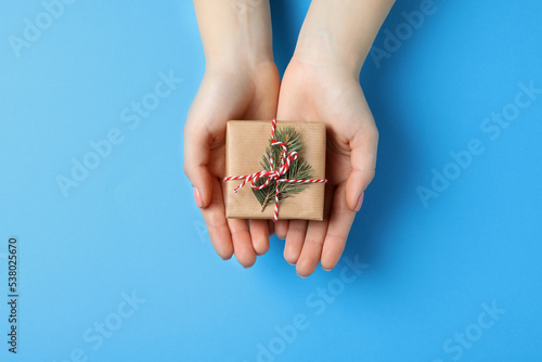 Christmas present. Woman holding beautifully wrapped gift box on light blue background, top view