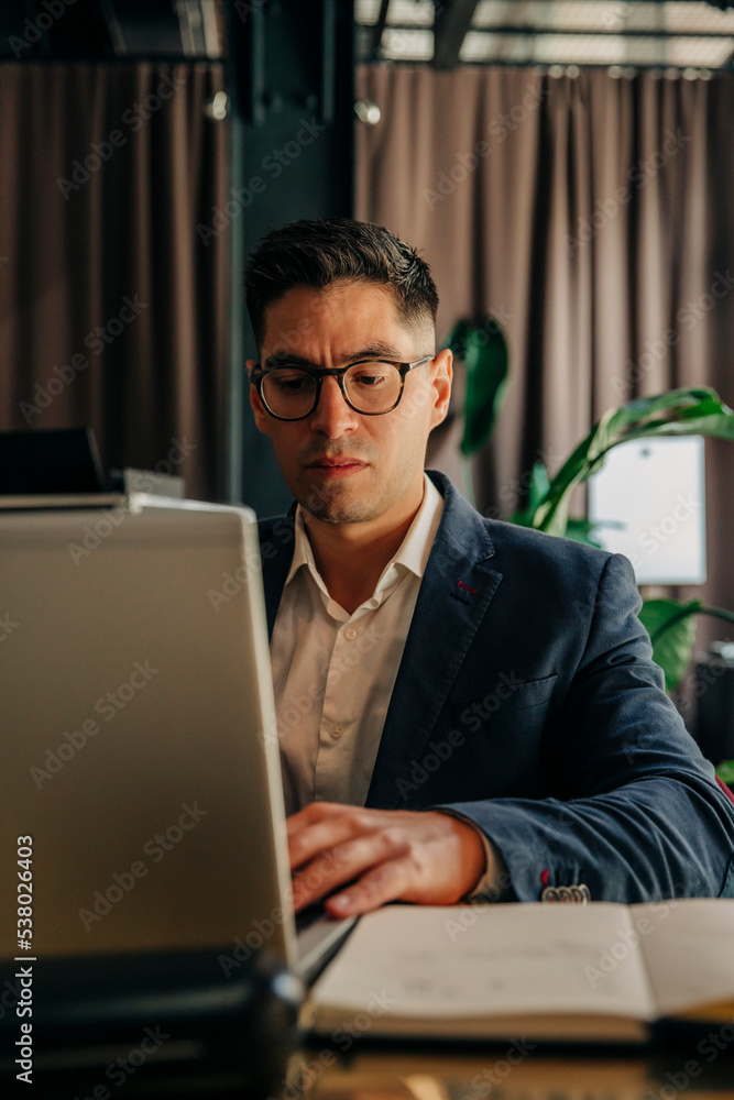 Mid adult businessman wearing eyeglasses using laptop while sitting in hotel lounge Mid adult businessman wearing eyeglasses using laptop while sitting in hotel lounge