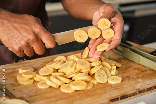 Slika na platnu Unrecognizable young african man cutting plantains in a kitchen.