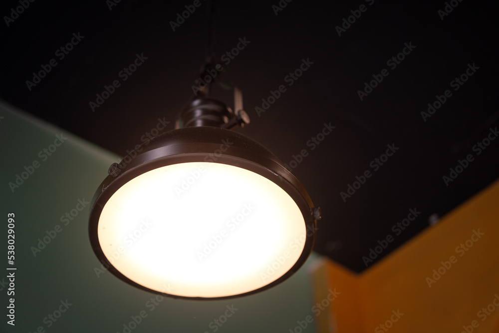 A metallic ceiling lighting lamp is glowing with yellow warm light shade. Interior decoration object equipment photo. Selective focus. A metallic ceiling lighting lamp is glowing with yellow warm light shade. Interior decoration object equipment photo. Selective focus.