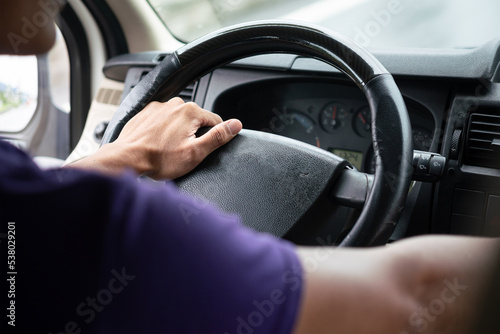 Action of a driver hand is holding and controlling on car's steering wheel during driving, photo from behind. Transportation occupation service with people part, selective focus. © Nattawit