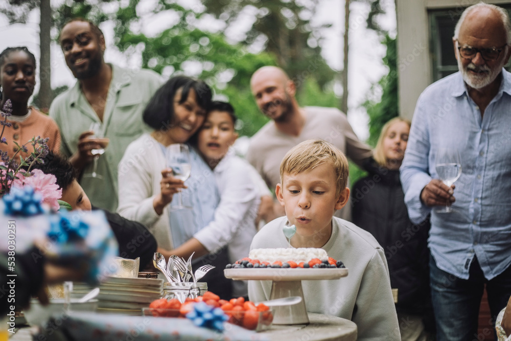Boy blowing candle on cake during birthday celebration with family Boy blowing candle on cake during birthday celebration with family