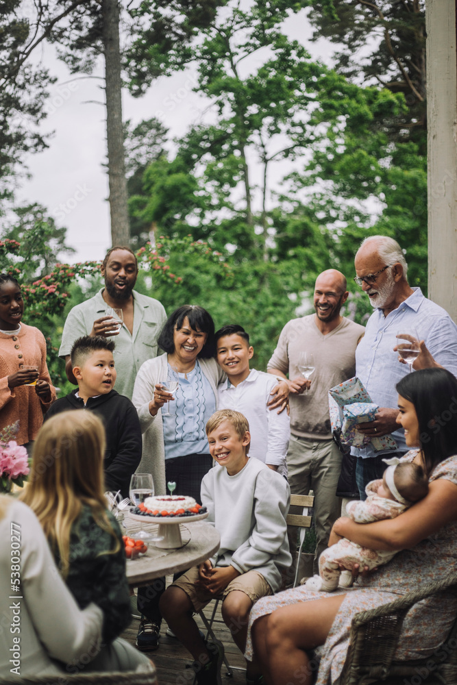Boy sitting on chair amidst happy family members during birthday celebration Boy sitting on chair amidst happy family members during birthday celebration