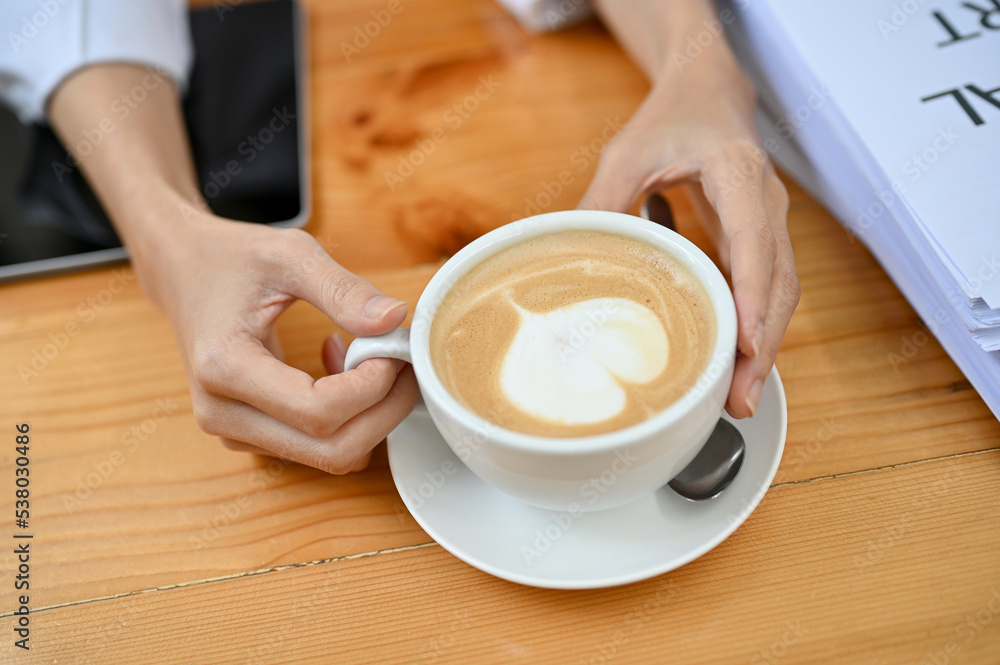 A female hands holding a cup of hot latte art on the table in the coffee shop. A female hands holding a cup of hot latte art on the table in the coffee shop.