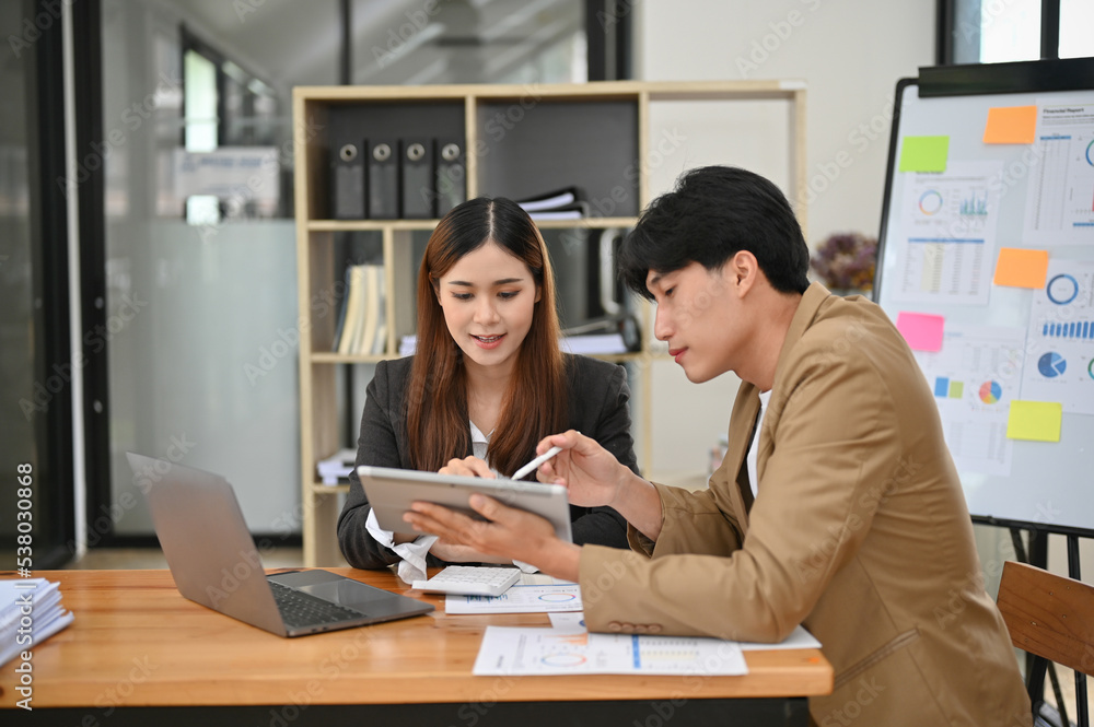 Charming Asian businesswoman looking at tablet screen, working with her male boss Charming Asian businesswoman looking at tablet screen, working with her male boss