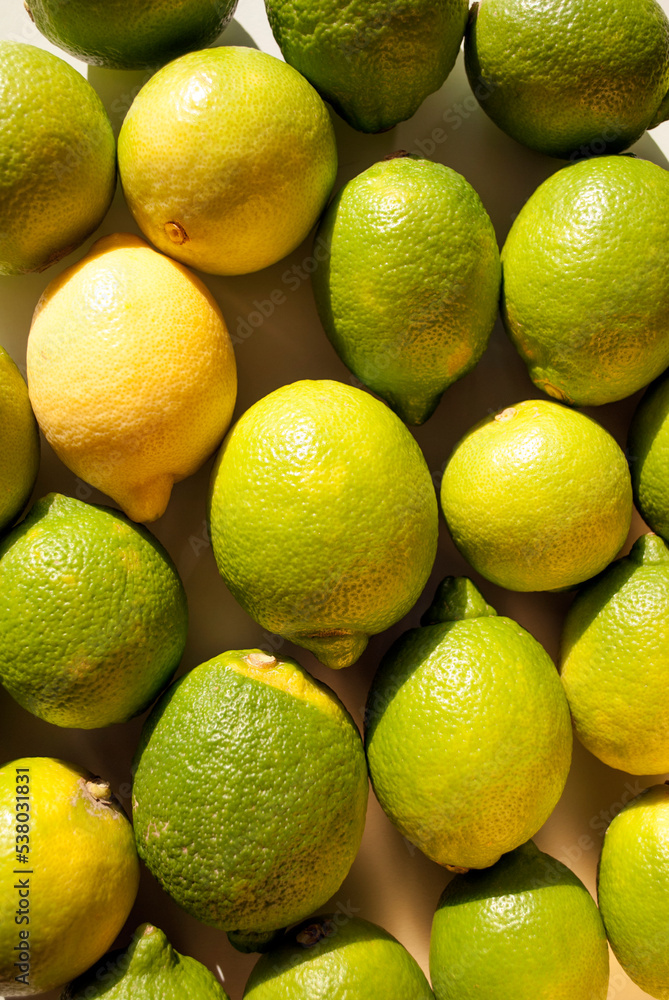 Overhead view of tight arrangement of yellow and green lemon fruit on gray background with hard shadows. Green living and eco-friendly products Overhead view of tight arrangement of yellow and green lemon fruit on gray background with hard shadows. Green living and eco-friendly products