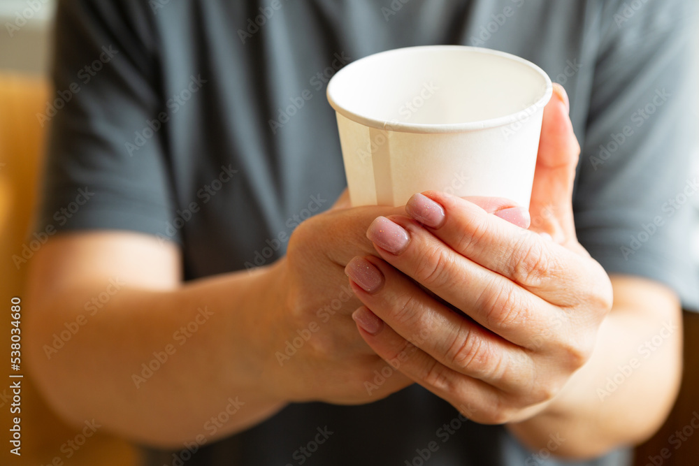 Female hands hold one white paper cup. Hot drink in hand. Warm up with a hot drink in a paper cup. Female hands hold one white paper cup. Hot drink in hand. Warm up with a hot drink in a paper cup.