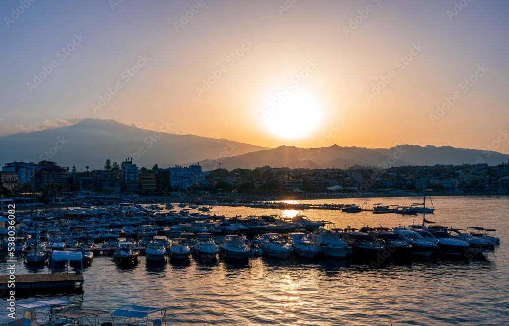Fototapeta premium picturesque sunrise or sunset in a sea port with a gulf dock pier with tour boats and a town with cloudy sky on background of a seashore landscape