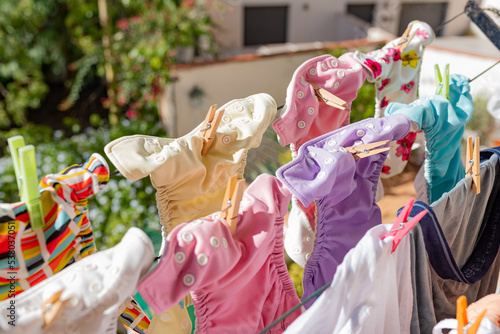 Cloth diapers hanging while drying under the sun on clothesline. Laundry of colorful reusable nappies for babies.