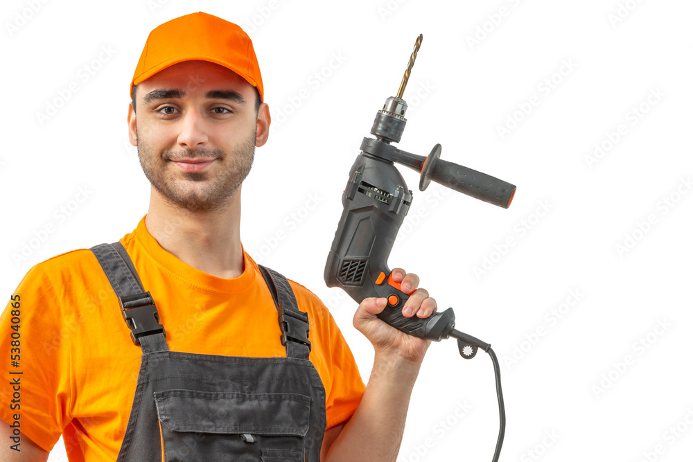 Young worker drilling with electric drill in his hands. Tool for boring holes. Craftsman repairman wearing orange uniform cap and t-shirt, overalls on a white isolated background for advertising Young worker drilling with electric drill in his hands. Tool for boring holes. Craftsman repairman wearing orange uniform cap and t-shirt, overalls on a white isolated background for advertising