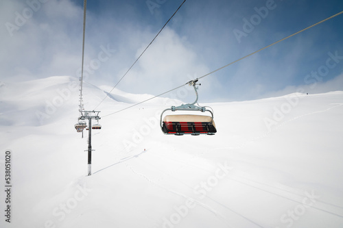 View from the outside of the aerial passenger line of a ski resort in winter in sunny weather against the backdrop of snow-capped mountains