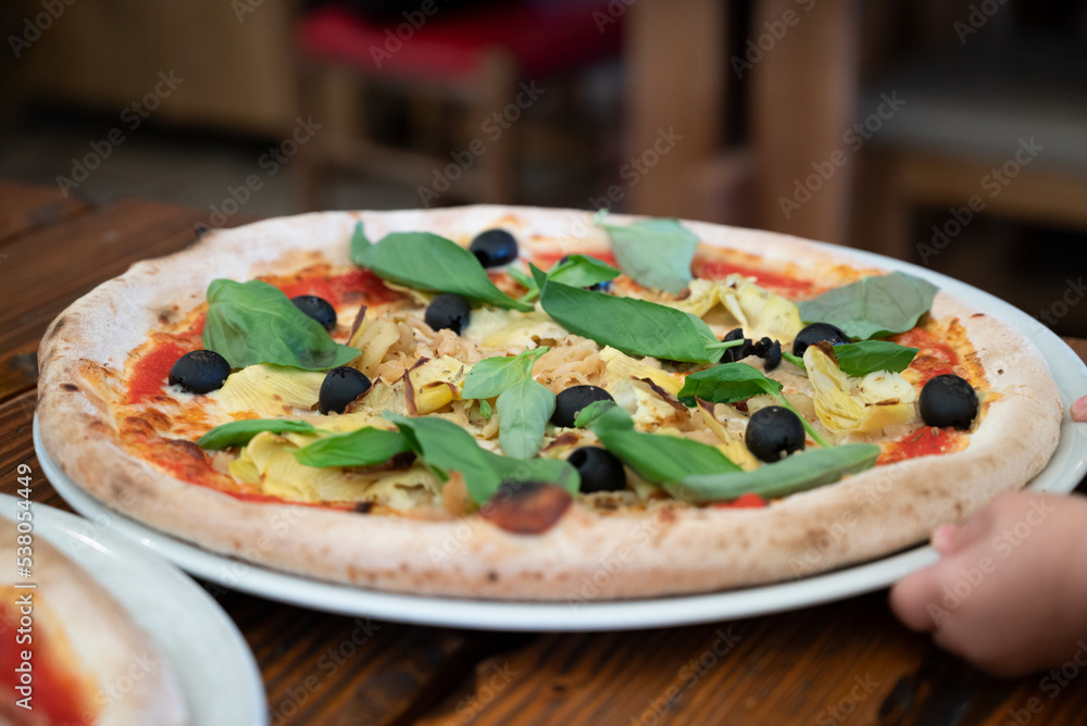 Fresh pizza with artichokes, black olives and basil leaves