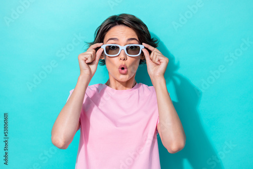 Photo of excited speechless staring girl with bob hairdo pink t-shirt hands hold sunglass impressed news isolated on teal color background