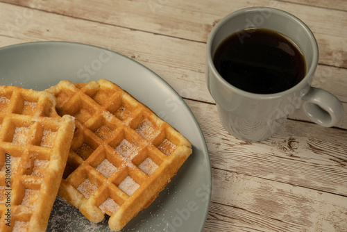 Plate with freshly baked waffles with a cup of black coffee on a light wooden background - breakfast, snack, pastry concept