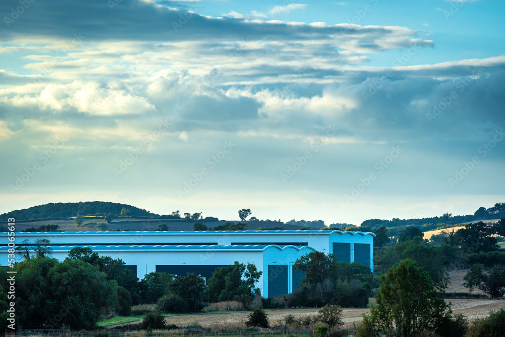 Obraz premium new built distribution warehouse building with farm fields in foreground in england uk