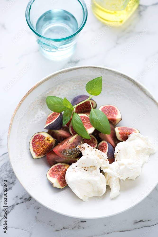 Salad with red tomatoes, fresh figs, mozzarella and green basil, vertical shot on a white marble background, elevated view Salad with red tomatoes, fresh figs, mozzarella and green basil, vertical shot on a white marble background, elevated view