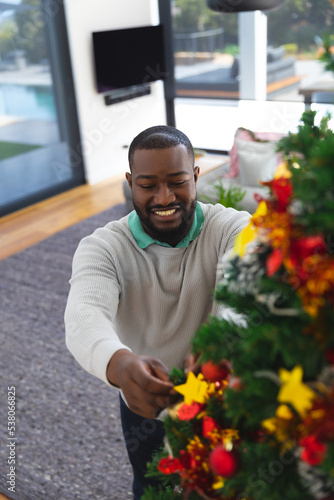 Happy african american man decorating christmas tree in living room
