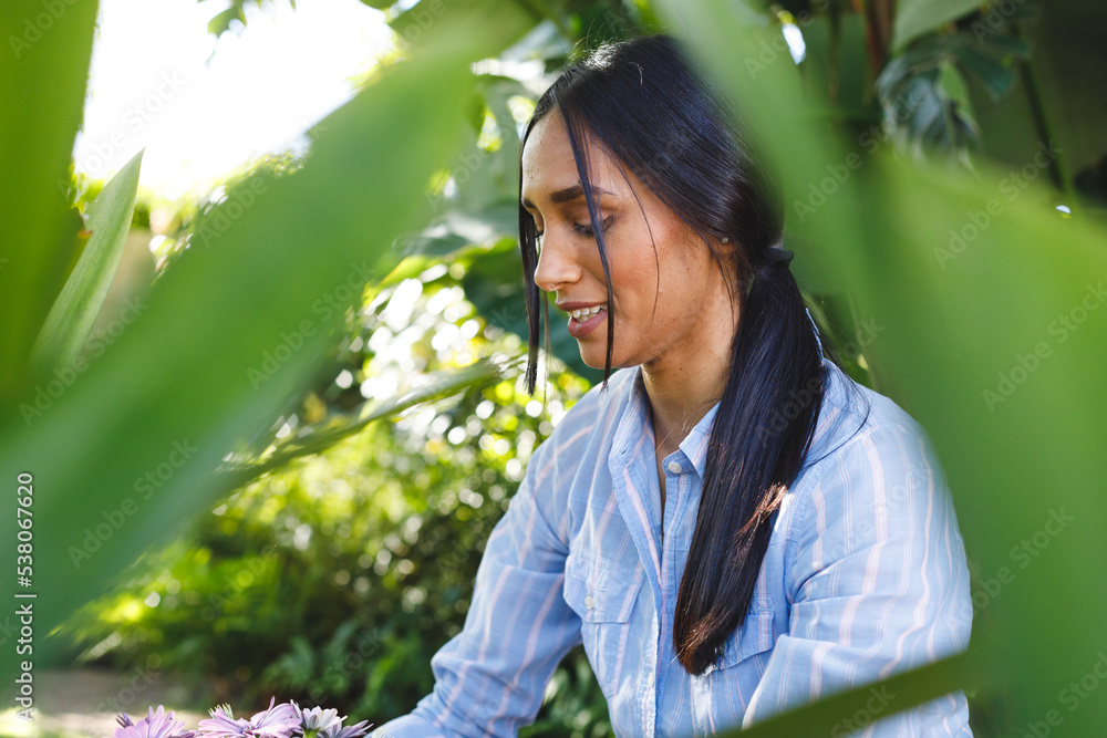 Happy biracial woman planting flowers in garden and smiling Happy biracial woman planting flowers in garden and smiling