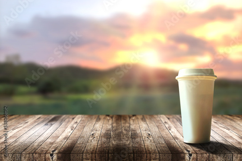 Hot coffee in a takeaway plastic cup on a brown wooden table with rural nature view and mountain with nice sky background and sunrise in morning, Refreshing drinks and relaxing in holiday.