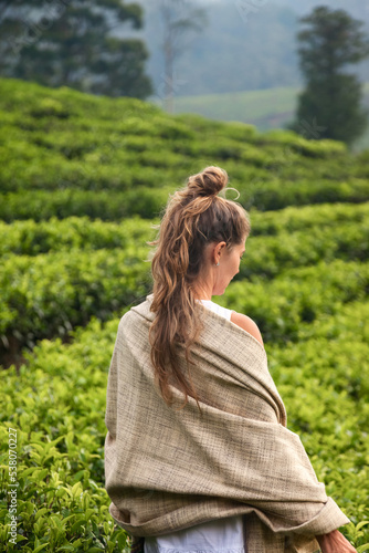 Rear view young woman in casual traditional white clothes at tea plantation background landscape in Sri Lanka. Portrait of adult female standing on tea plant. Eco friendly concept. Copy text space