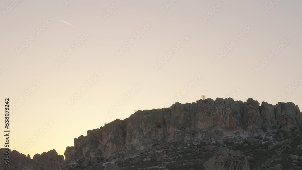 Kırkinler Rock Settlement, rock mountains at sunset and the white trail left behind by the flying plane. Kırkinler Rock Settlement, rock mountains at sunset and the white trail left behind by the flying plane.