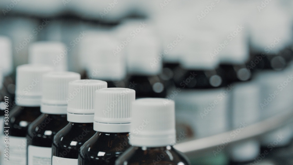 Glass bottles with white plastic caps moves to the packing on the pharmaceutical production line. Row on a conveyor in a manufacturing plant. Conveyor Provides Automated Processes. Depth of field Glass bottles with white plastic caps moves to the packing on the pharmaceutical production line. Row on a conveyor in a manufacturing plant. Conveyor Provides Automated Processes. Depth of field