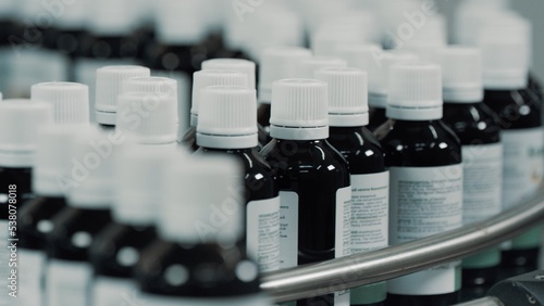 Glass bottles with white plastic caps moves to the packing on the pharmaceutical production line. Row on a conveyor in a manufacturing plant. Conveyor Provides Automated Processes. Depth of field
