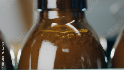 A row of glass bottles drive up and fill up with a liquid agent on a factory line. Manufacture drugs for medical supplies of pharmacy industry. Automatic bottling line. Close up