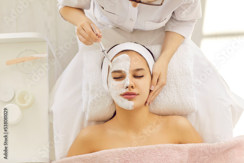 Top view of cosmetologist apply face mask on female client do procedures in spa or saloon. Beautician make facial treatment to woman in medical aesthetic clinic. Skincare, cosmetology and beauty.