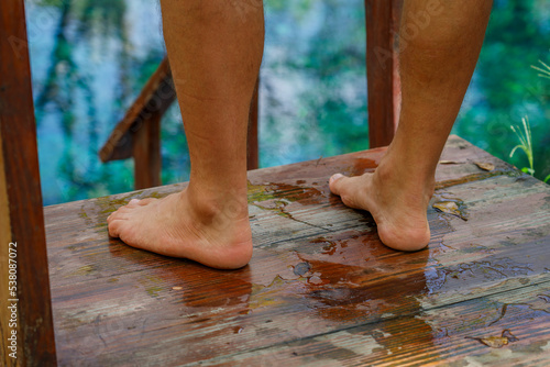 Men's feet stand on the pier while relaxing on the shore of a tropical lake.