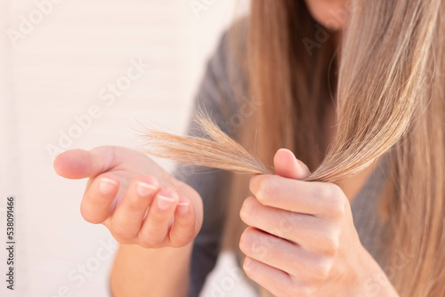 Close up view of unrecognizable woman holding damage hair with split ends with selective focus and blurred background