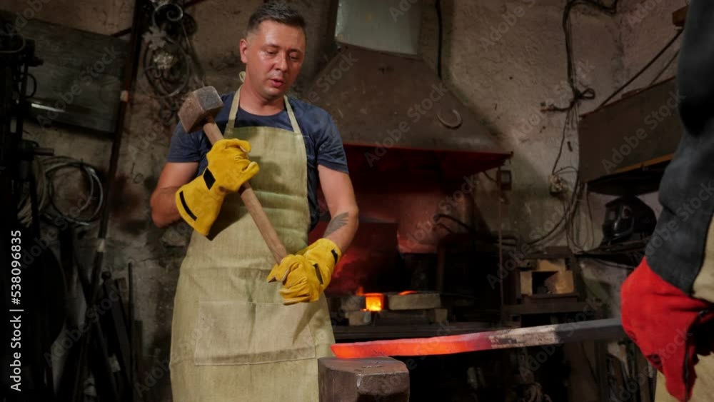 A strong brutal blacksmith manually molten metal on an anvil in