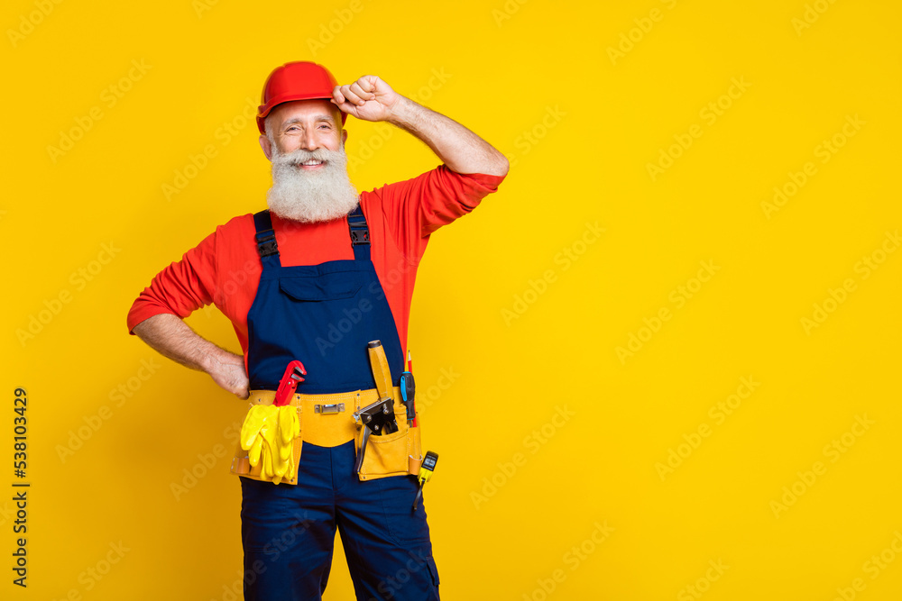 Photo portrait of nice grandpa craftsman arm touch helmet cheerful professional dressed safety uniform isolated on yellow color background Photo portrait of nice grandpa craftsman arm touch helmet cheerful professional dressed safety uniform isolated on yellow color background