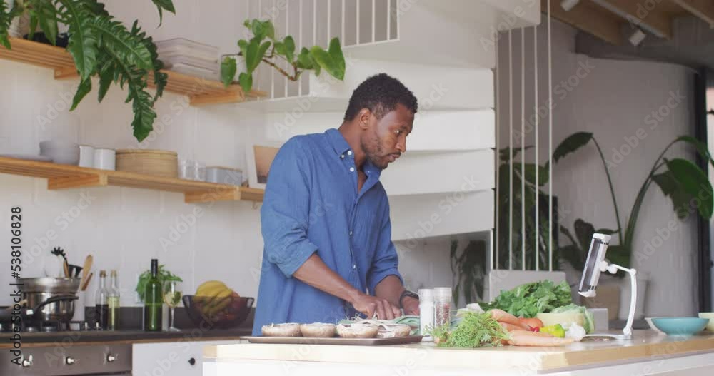 Happy african american man cooking dinner in kitchen, using tablet Happy african american man cooking dinner in kitchen, using tablet