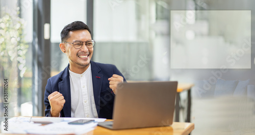 Excited happy businessman looking at the laptop screen, celebrating an online win, overjoyed young asian male screaming with joy, isolated over a white blur background