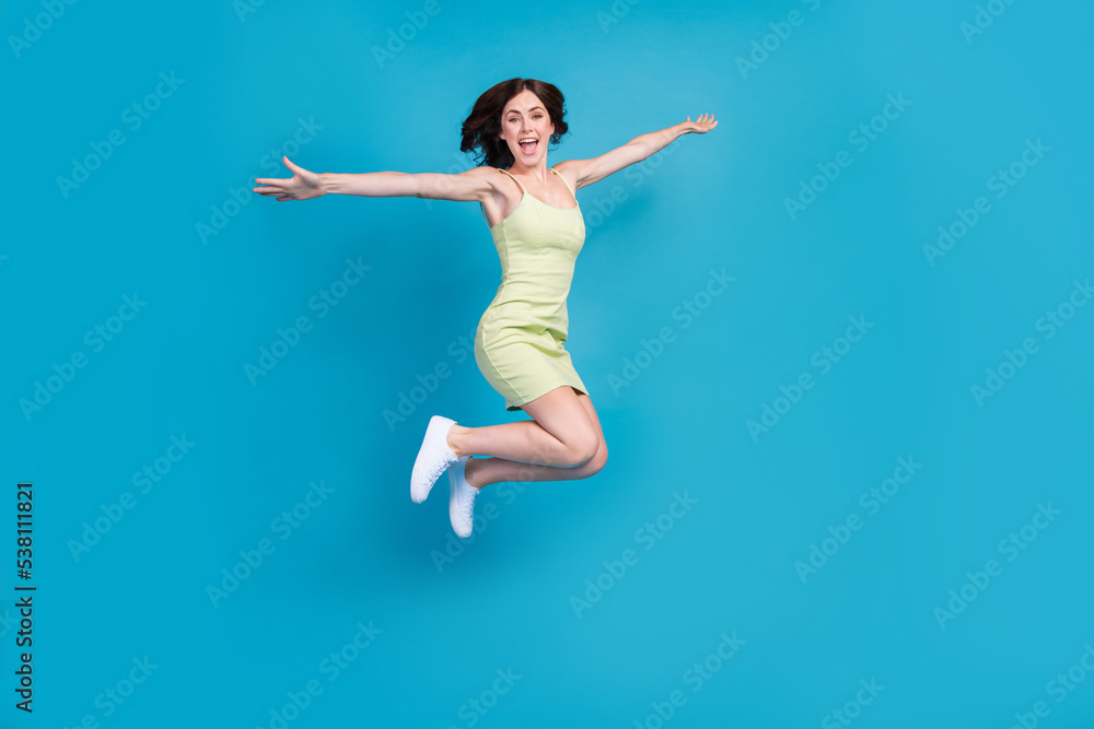 Full length photo of cute excited lady wear green outfit jumping high arms sides empty space isolated blue color background
