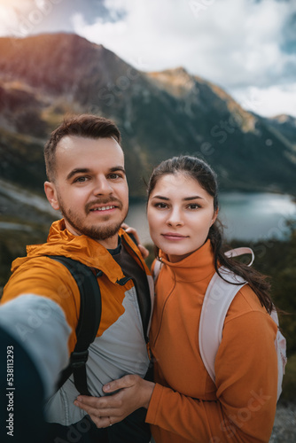 The young couple smiles and looks at the camera with a beautiful mountain and lake background. Family outdoor sports activity in the Tatra Mountains and Morskie Oko