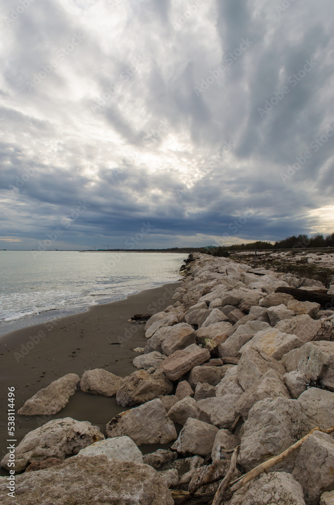 I murazzi, tipici sbarramenti di pietre, sulla spiaggia del Lido di Venezia in una giornata invernale con il cielo pieno di nuvole grigie